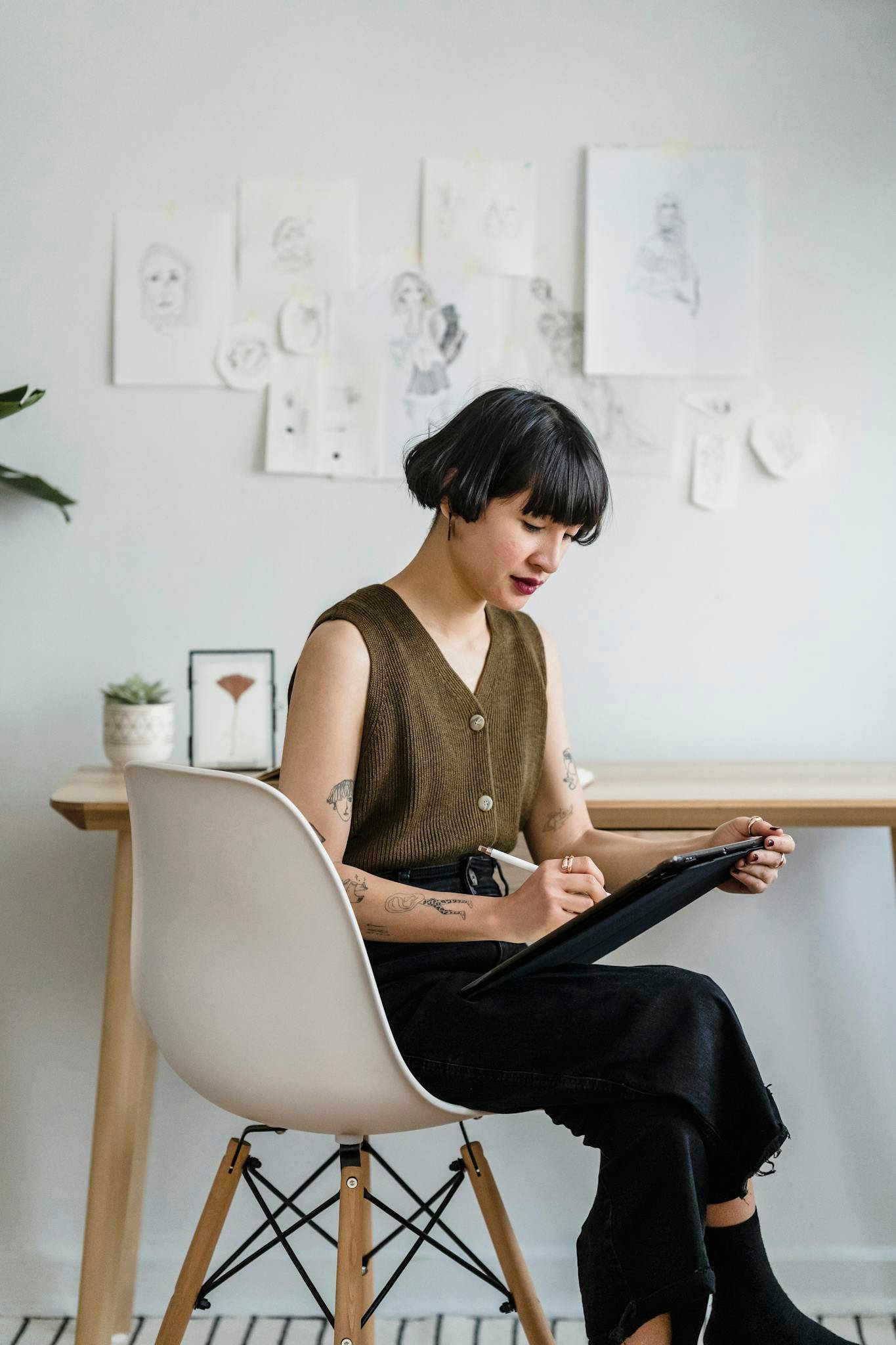 A young woman artist sketching on a tablet in a modern office setting, surrounded by artwork. Creative and focused atmosphere.