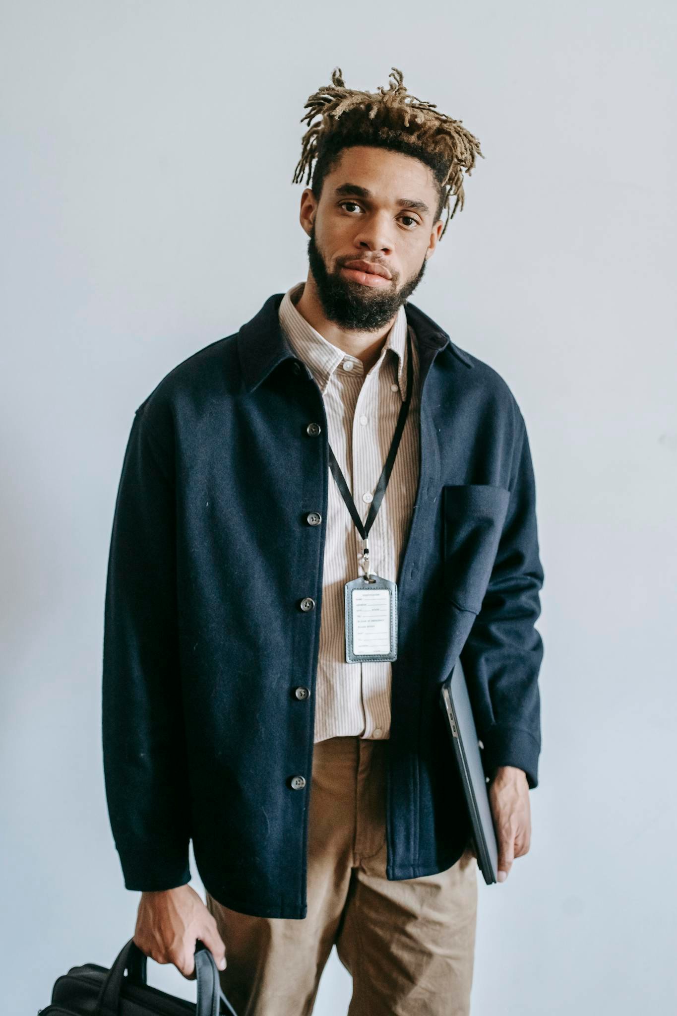 Portrait of a confident young African American man with laptop and bag, standing indoors.